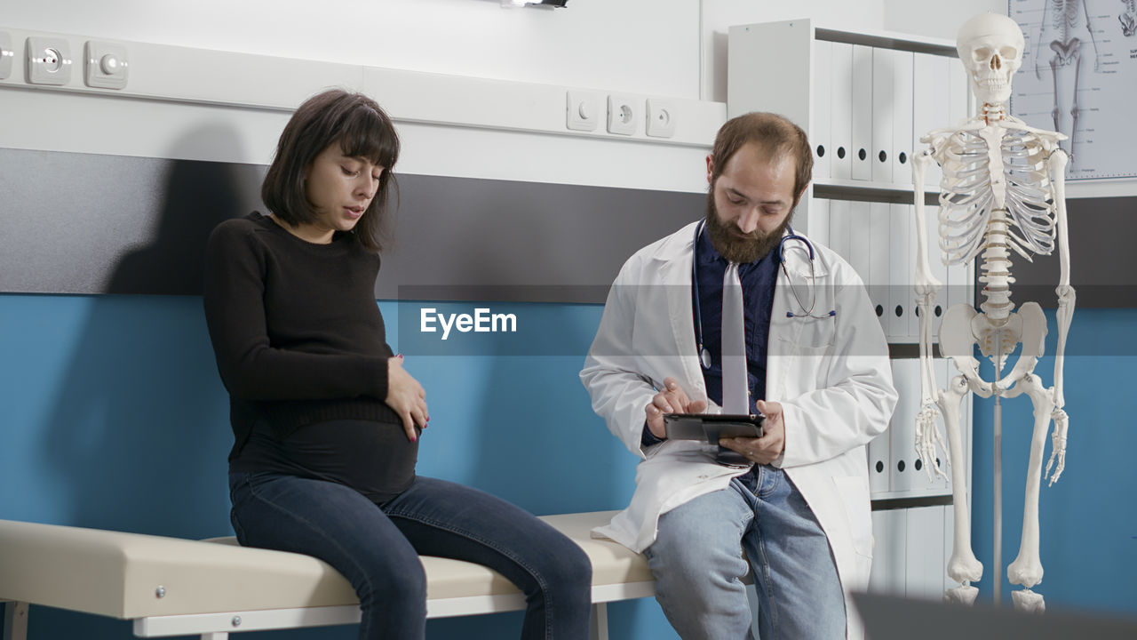 Doctor using digital tablet sitting by patient in hospital