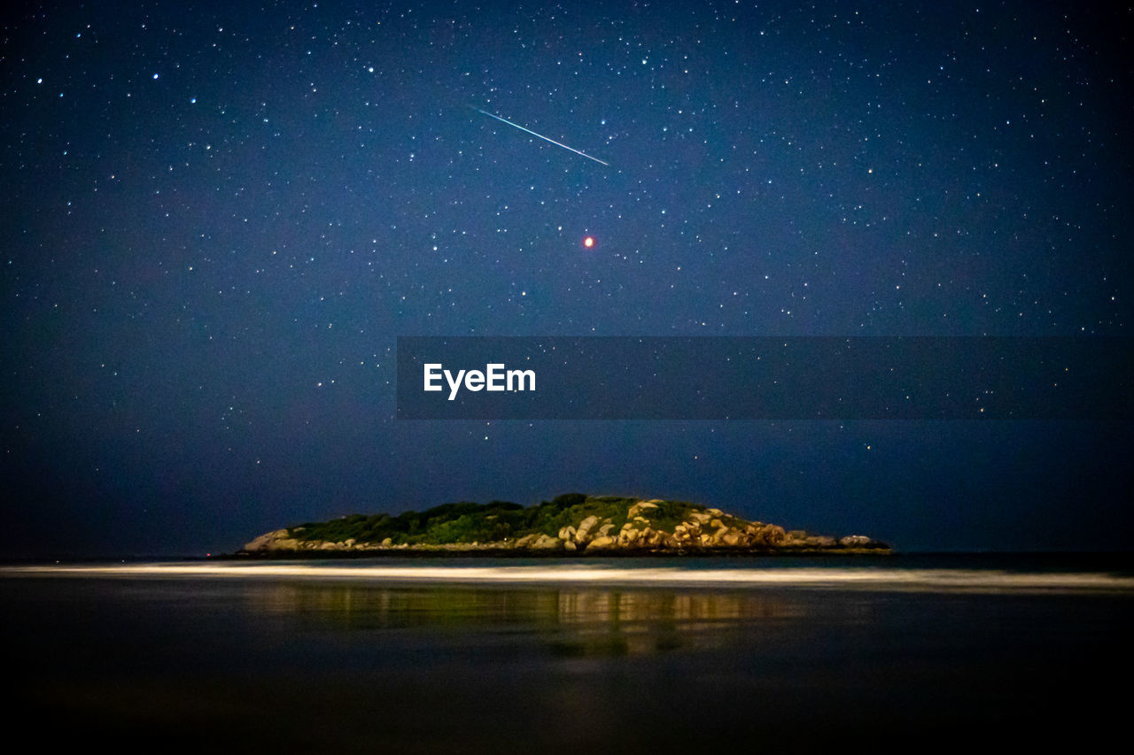 Meteor shooting through the night sky above island in ocean and mars.