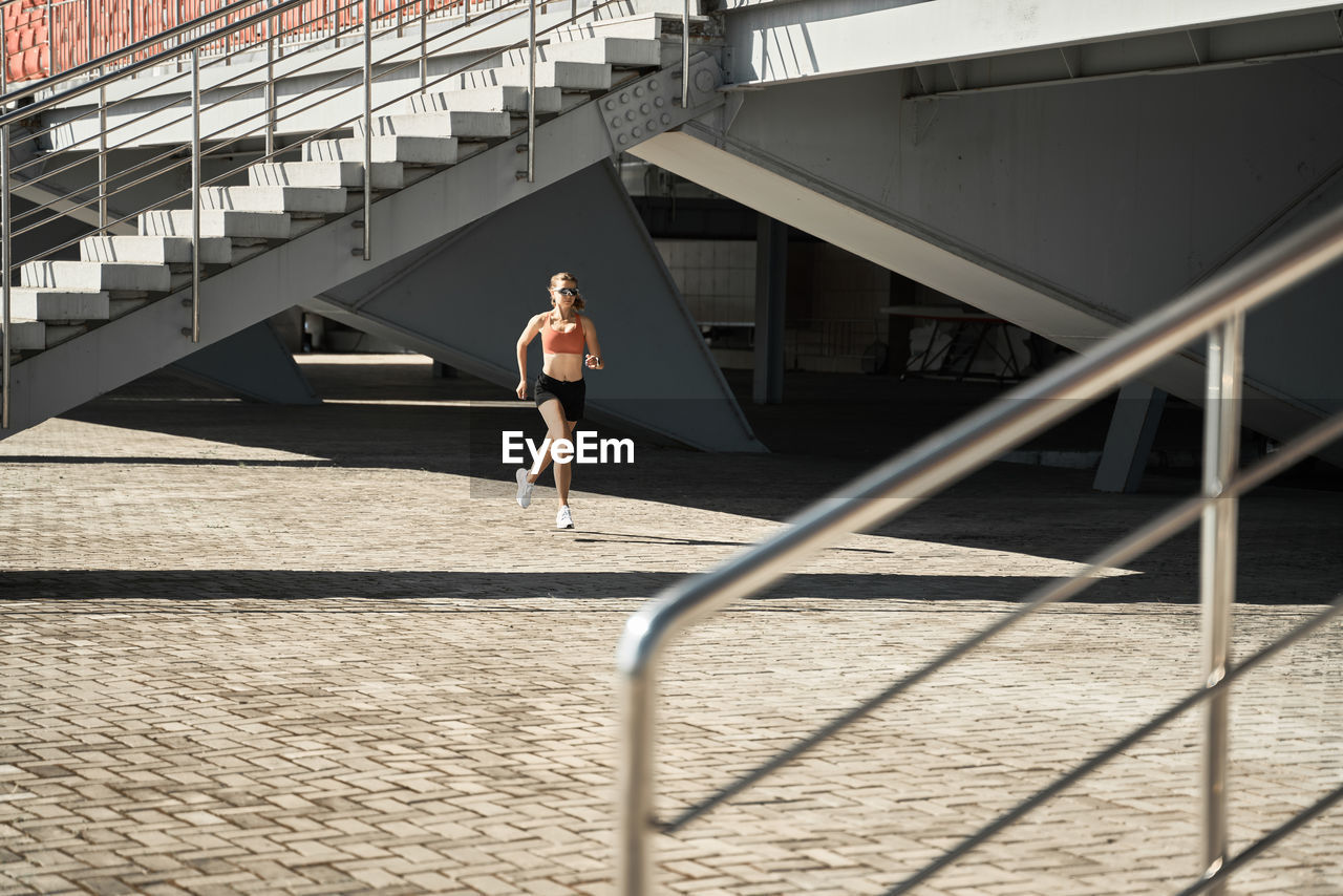 Side view of determined female athlete running fast during outdoor workout near stairways of stadium