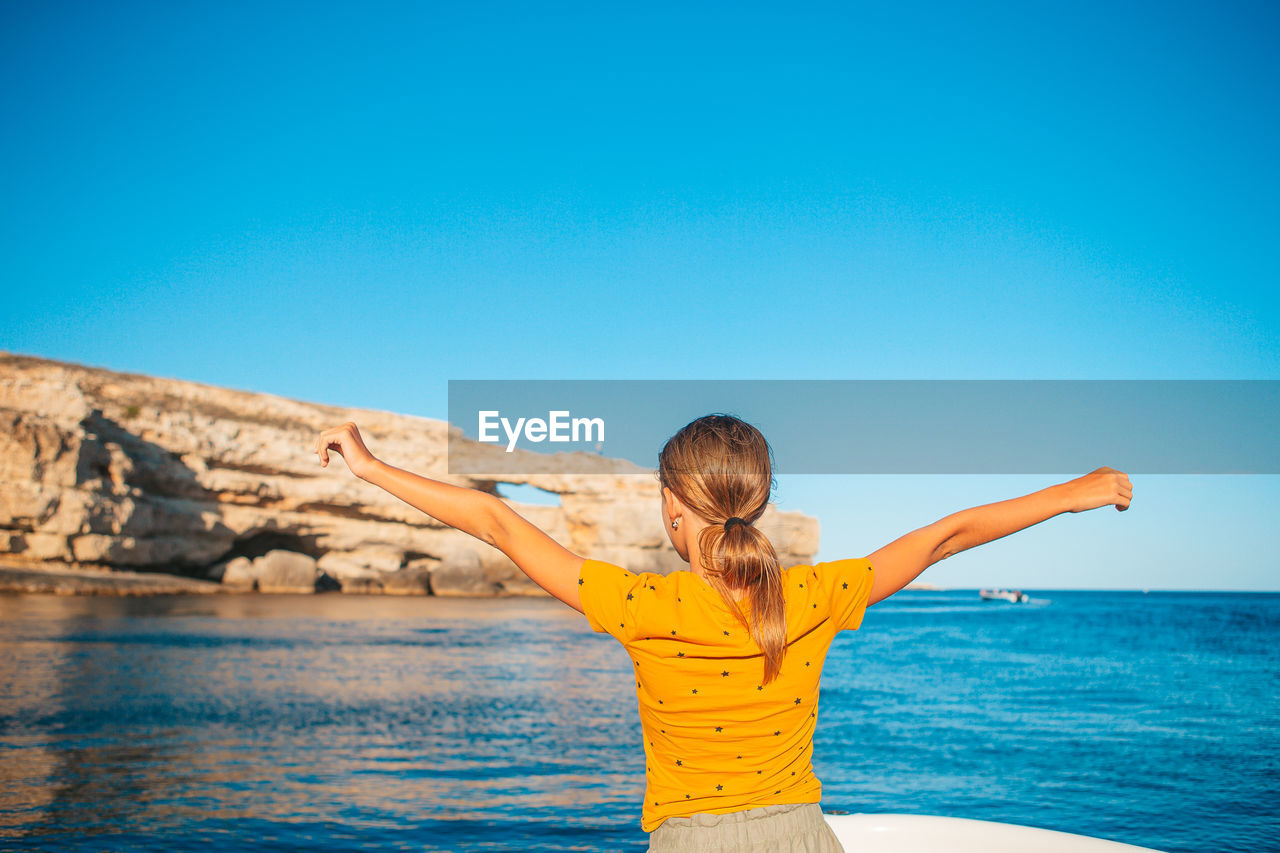 Rear view of woman standing by sea against clear blue sky