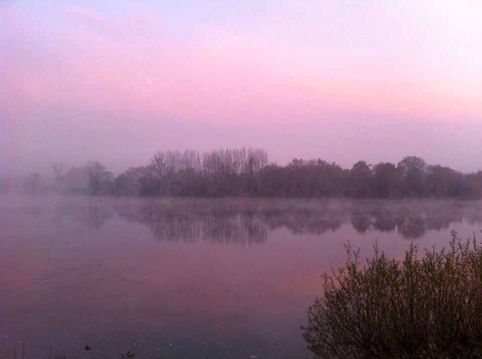 Scenic view of lake against sky during foggy weather at dusk