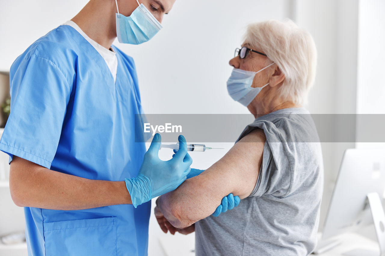 Doctor wearing mask vaccinating patient at hospital