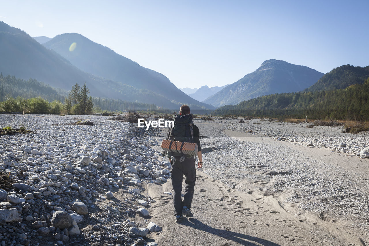 Hiker with backpack walking towards karwendel mountains, rissbach, vorderriss, bavaria, germany