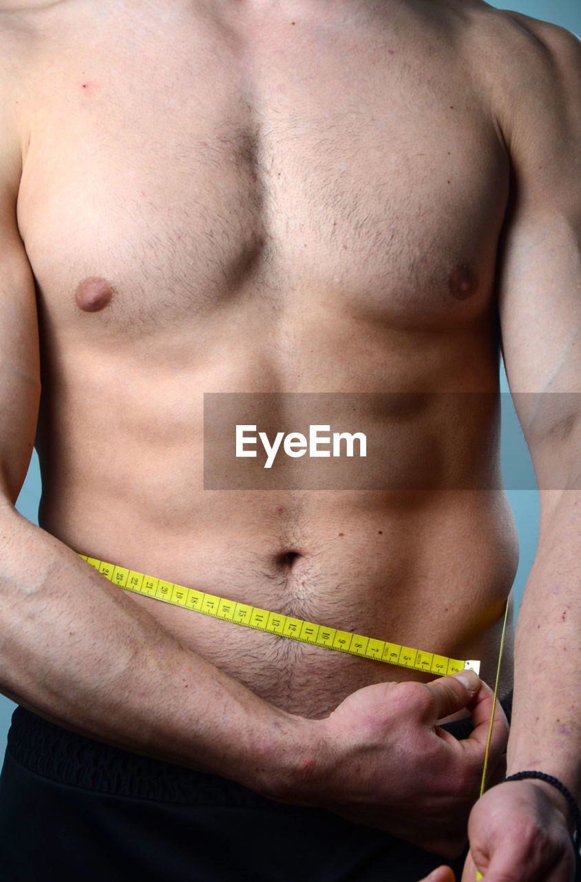 Midsection of shirtless man with tape measure