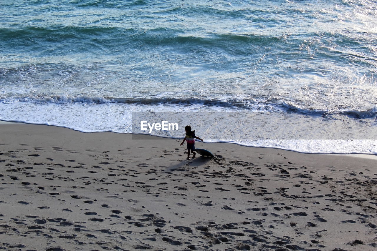 High angle view of boy walking with surfboard at beach