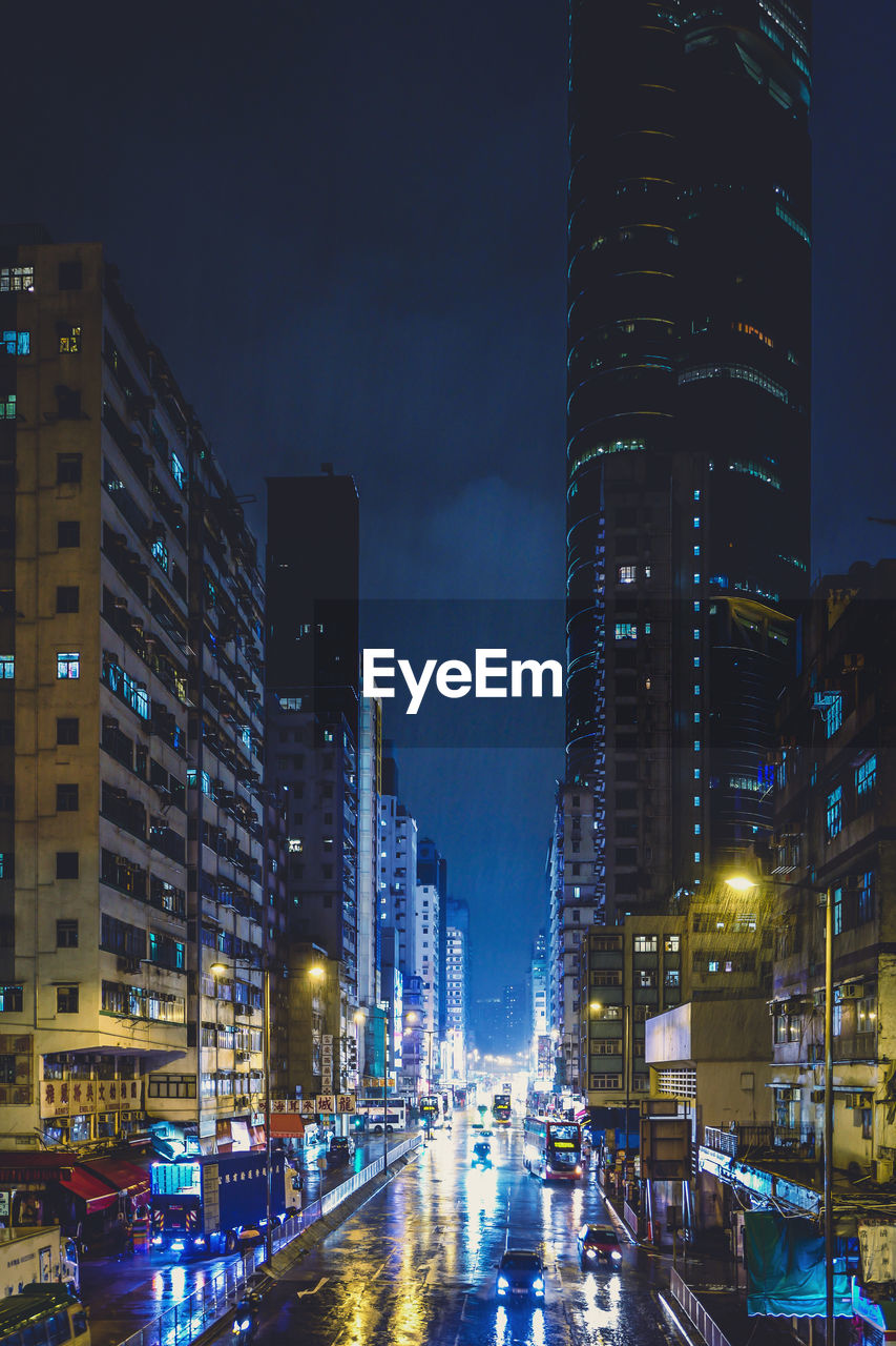 Illuminated street amidst buildings against sky at night