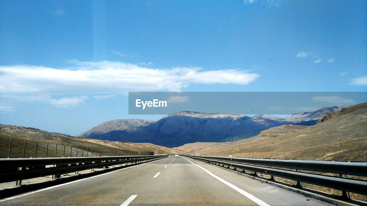 Country road leading towards mountains against blue sky