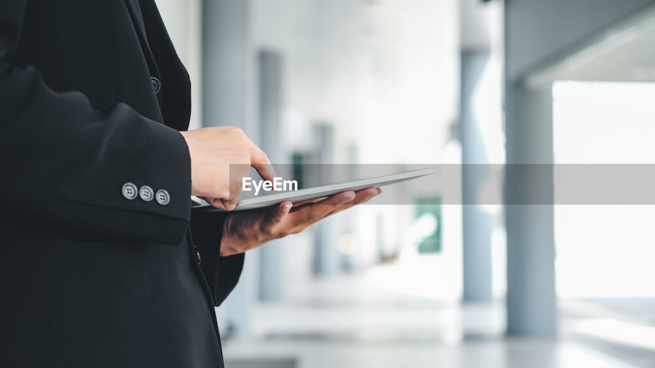 MIDSECTION OF MAN USING MOBILE PHONE IN OFFICE