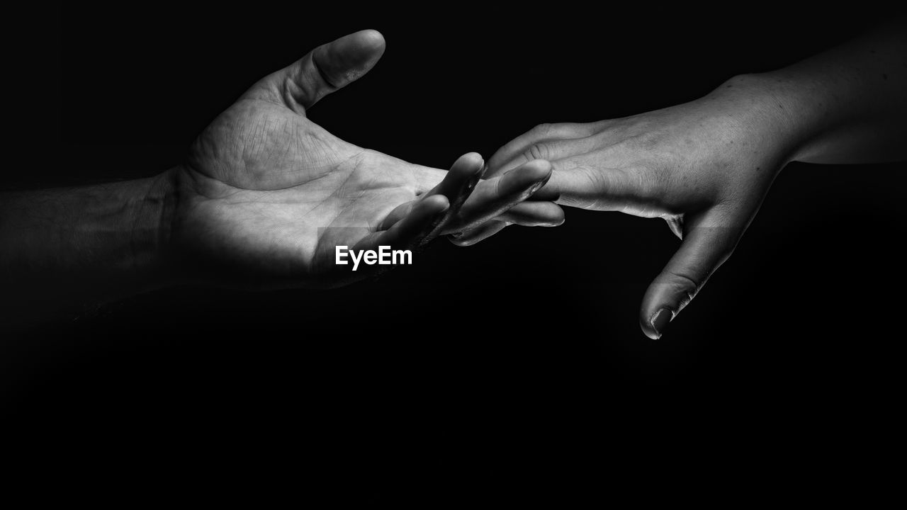 Close-up of couple holding hands against black background