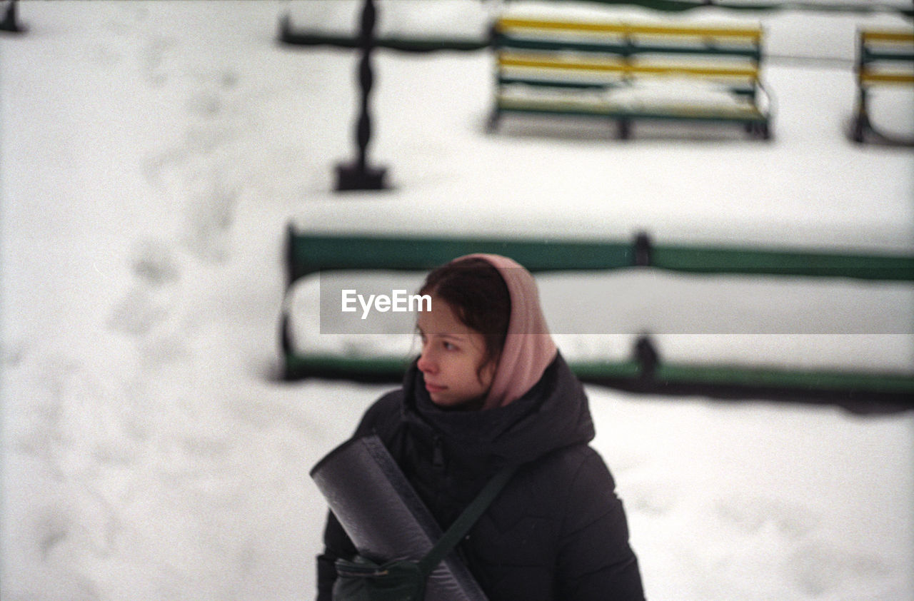 Young woman looking away while standing outdoors during winter