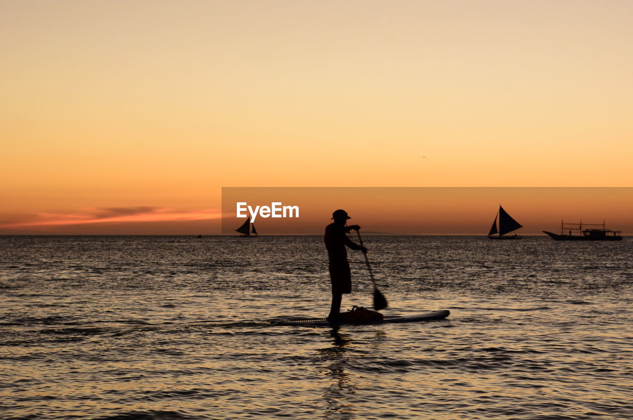 SILHOUETTE MAN ON SEA AGAINST ORANGE SKY