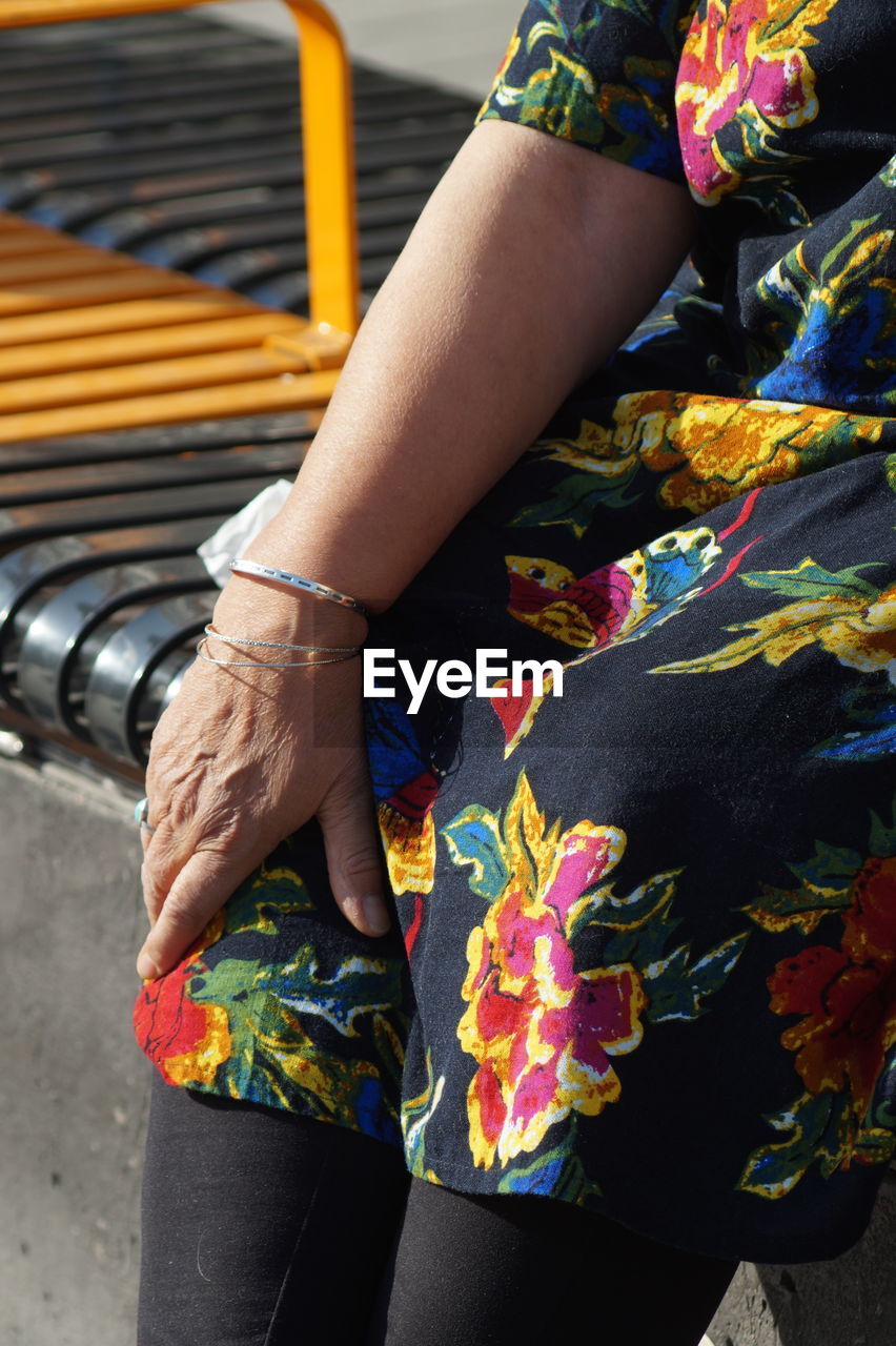 Midsection of woman sitting on bench in city