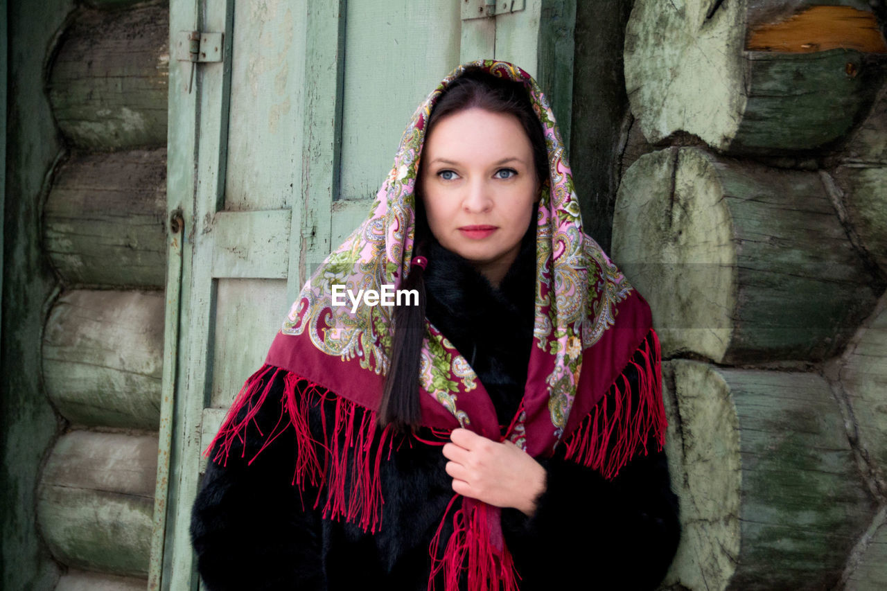 Woman wearing scarf looking away against log cabin