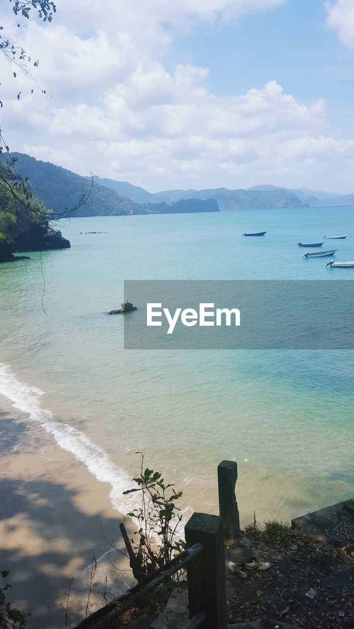 BOATS IN SEA WITH MOUNTAIN RANGE IN BACKGROUND