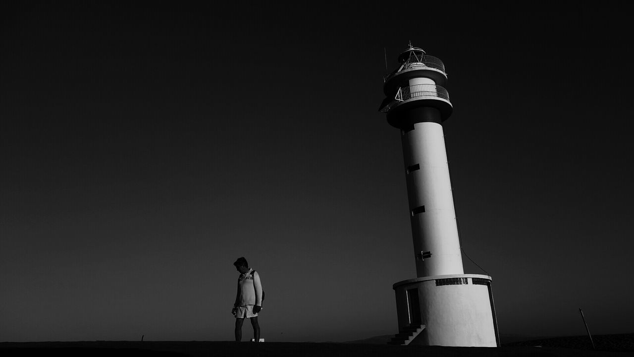 Man standing by lighthouse against clear sky