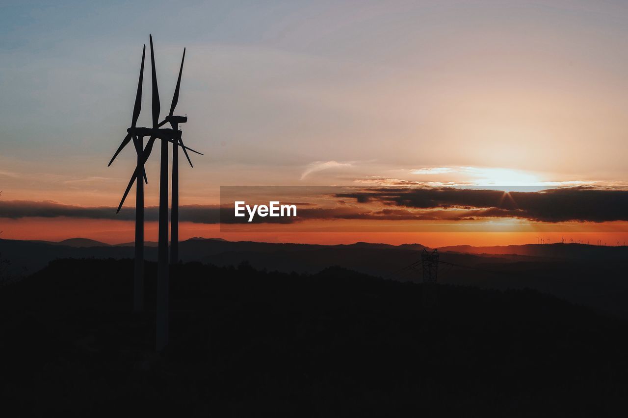 Silhouette electricity pylon against dramatic sky during sunset