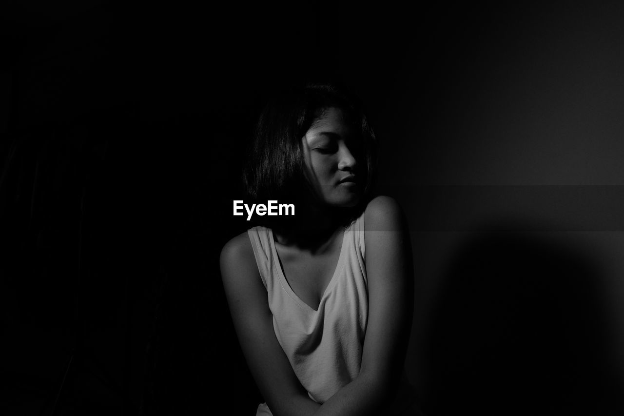 Young woman sitting against black background