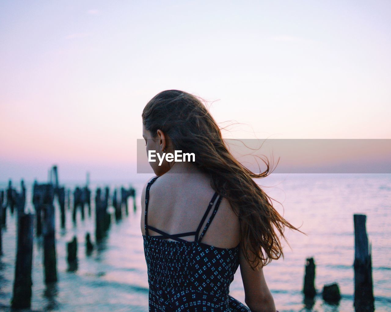 Woman sitting in sea against sky during sunset