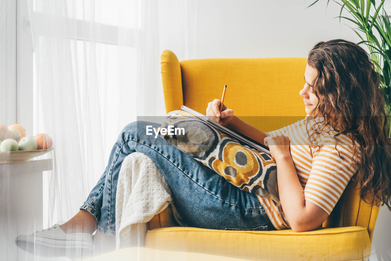 young woman using mobile phone while lying on sofa at home