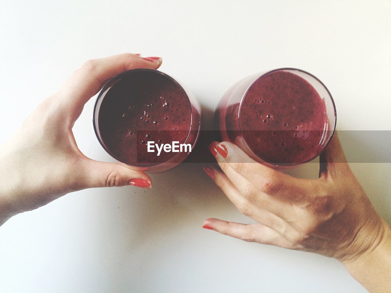 Cropped hands of friend holding smoothies on table