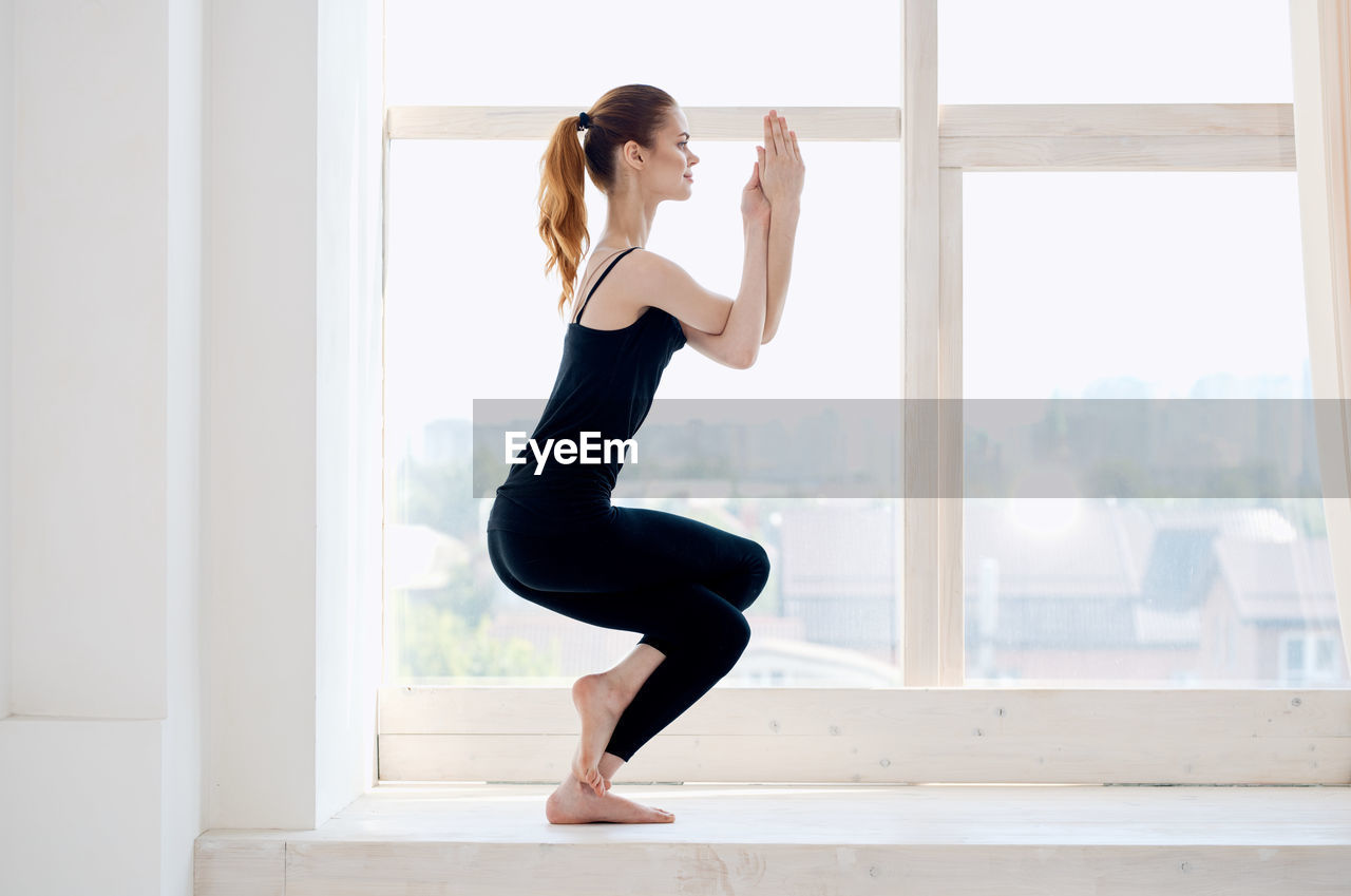Full length side view of woman exercising in window at home