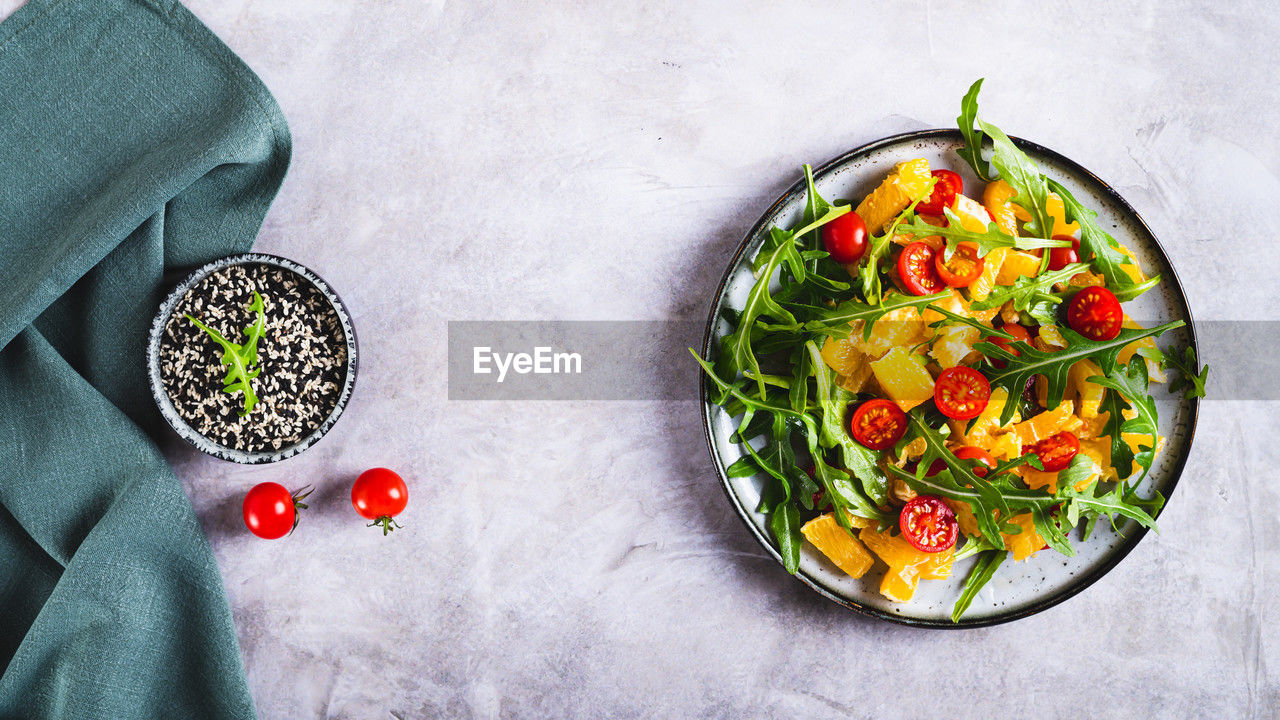 Dietary salad of orange slices, cherry tomatoes and arugula on a plate top view web banner