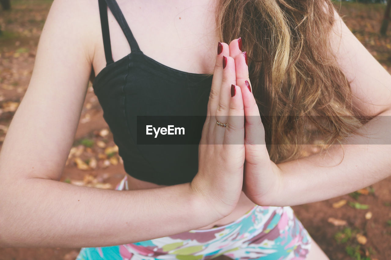 Midsection of young woman doing yoga with hands clasped on field