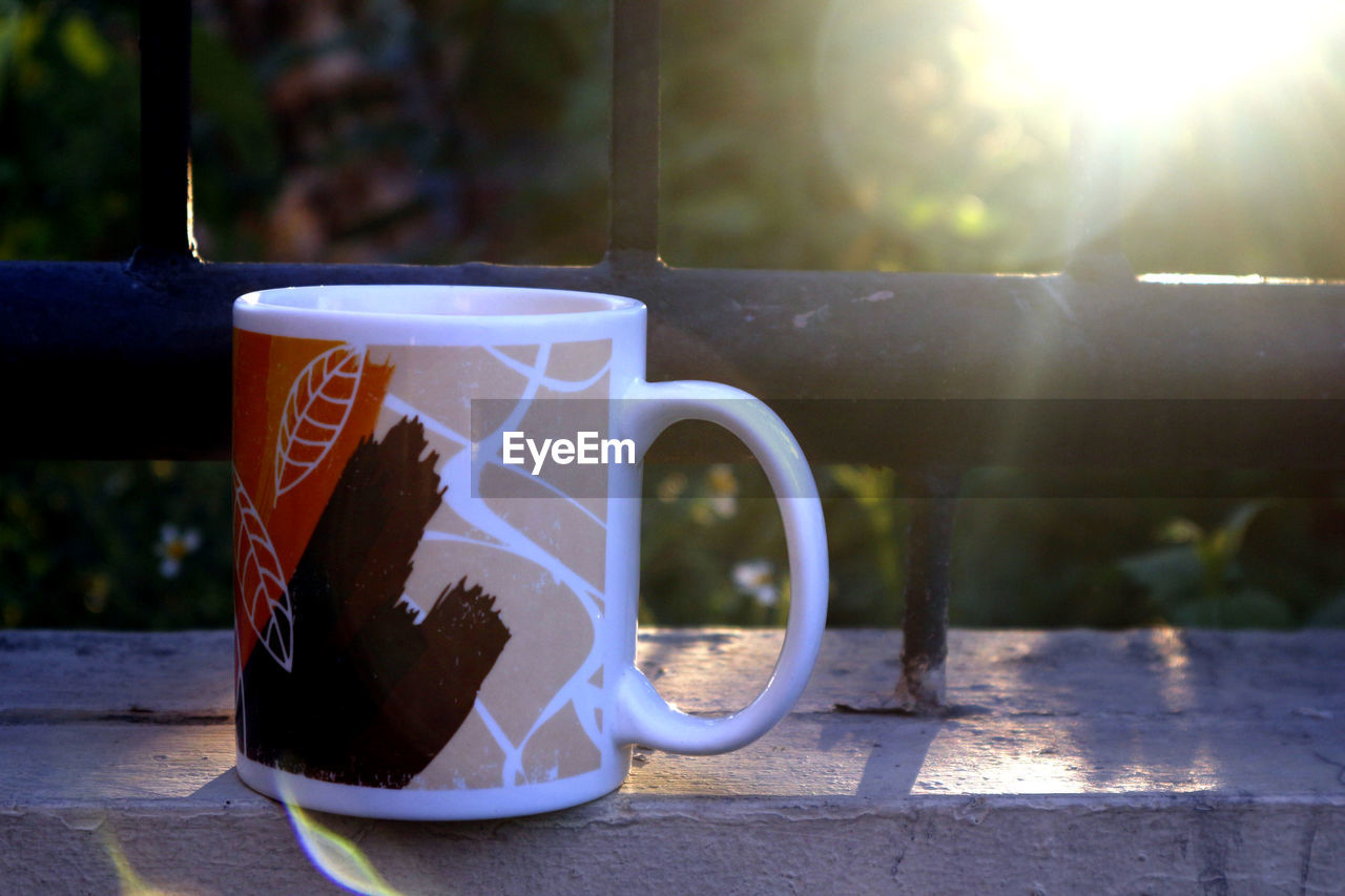 Photo of a coffee mug on a fence with beautiful sunset in the background.