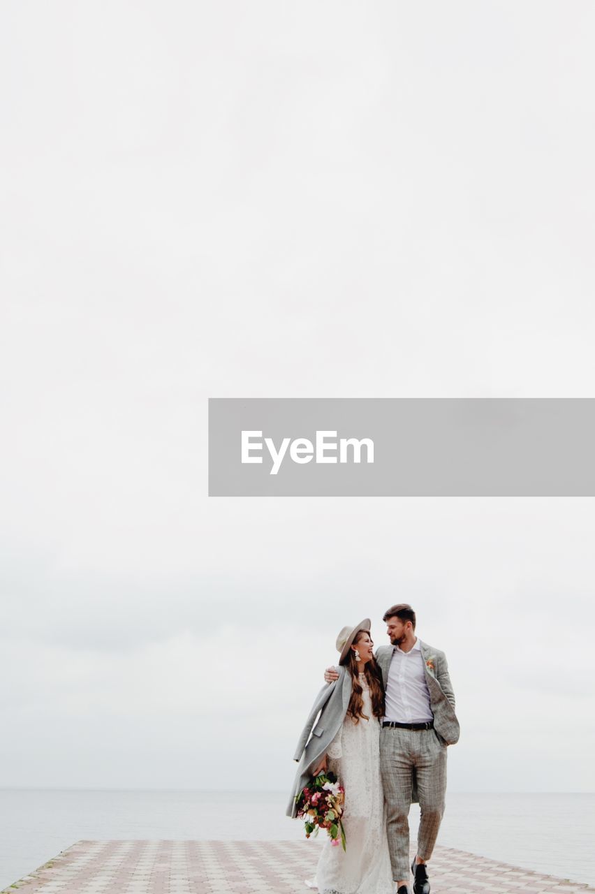 Bride and bridegroom walking on pier in sea during wedding ceremony