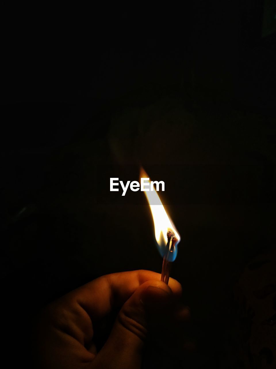 Close-up of hand holding burning matchstick over black background