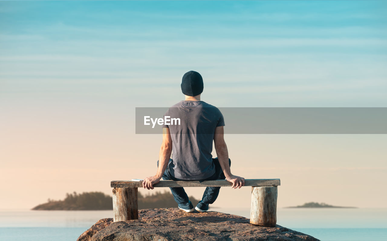 Rear view of man looking at sea against sky during sunset