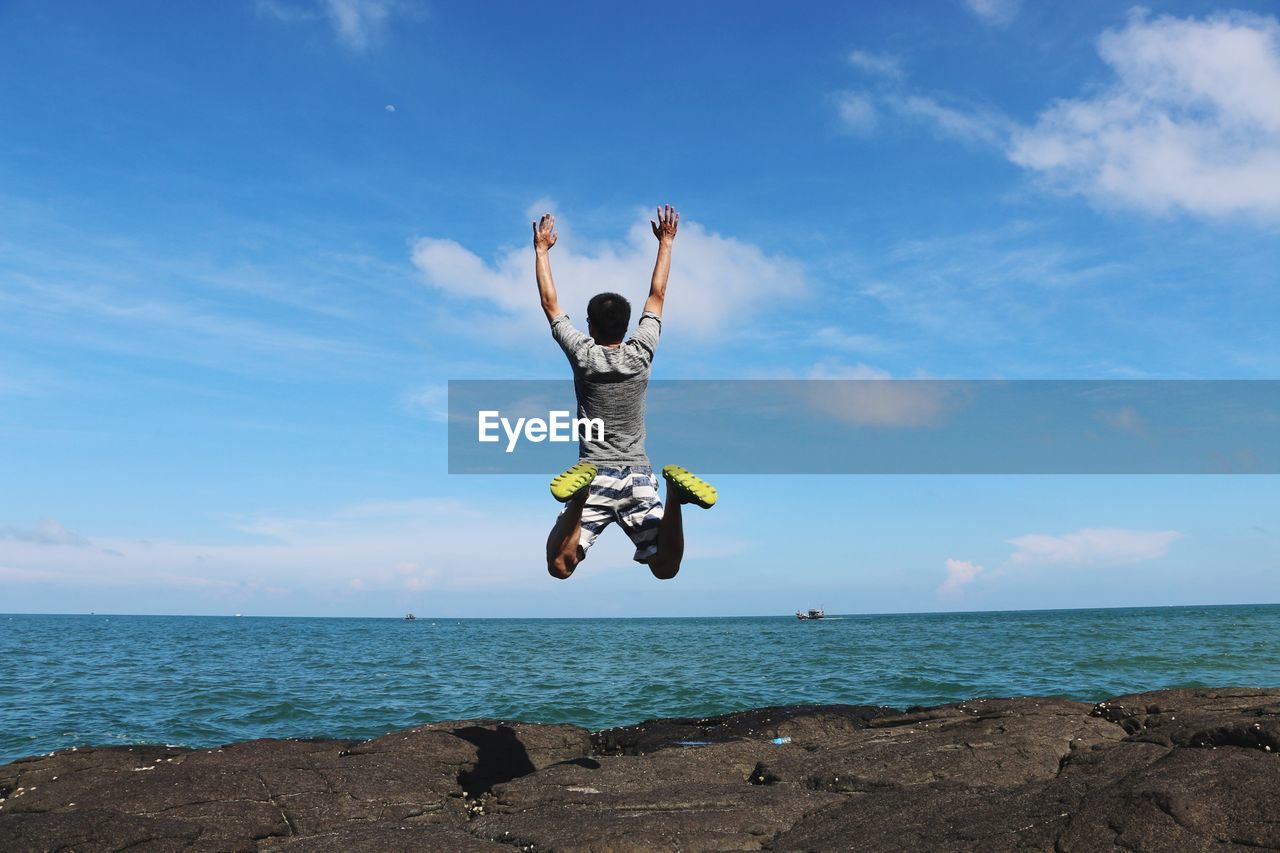 Man jumping over sea against blue sky