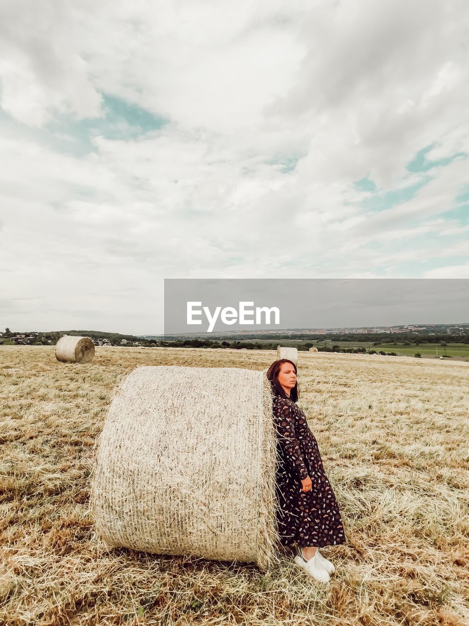 Woman standing by hay bales on field against sky