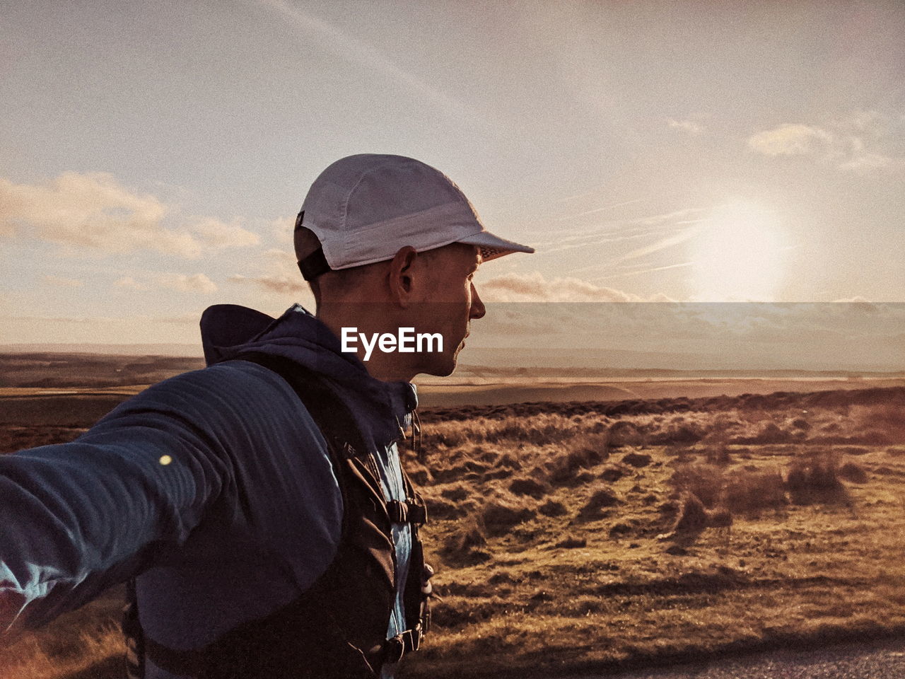 Side view of young man on land against sky during sunset