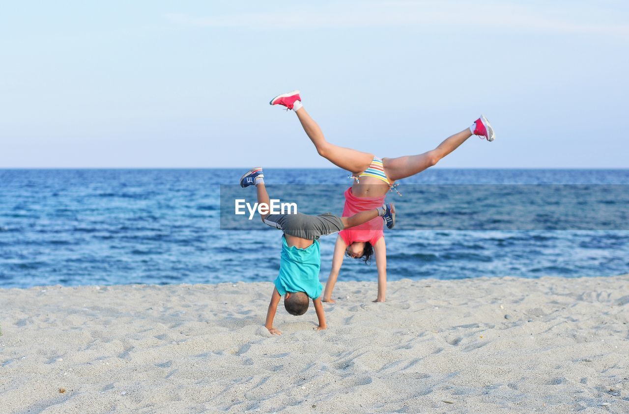 Children doing handstand on sand at beach against sky