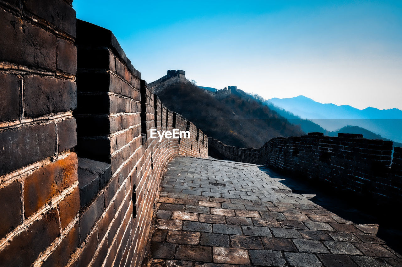 architecture, sky, rock, mountain, nature, wall, history, built structure, travel destinations, landscape, the past, travel, scenics - nature, environment, brick, blue, no people, clear sky, ancient, outdoors, mountain range, city, tourism, building exterior, beauty in nature, building, sunlight, footpath, fort, stone material, tranquility, reflection, sunny, brick wall, surrounding wall, old, staircase, terrain, land