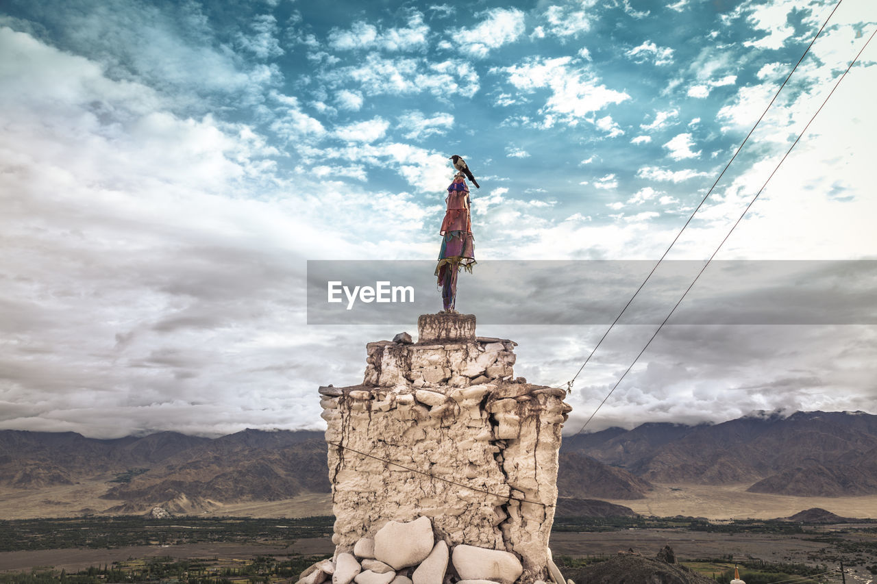 Crow sitting on the sculpture on rock against sky