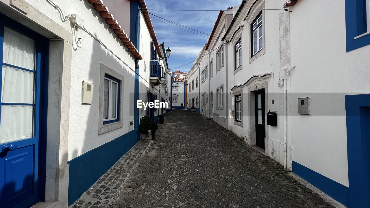 architecture, building exterior, blue, built structure, alley, road, street, building, city, house, town, window, urban area, residential district, sky, lane, infrastructure, day, nature, the way forward, neighbourhood, no people, outdoors, facade, diminishing perspective, transportation