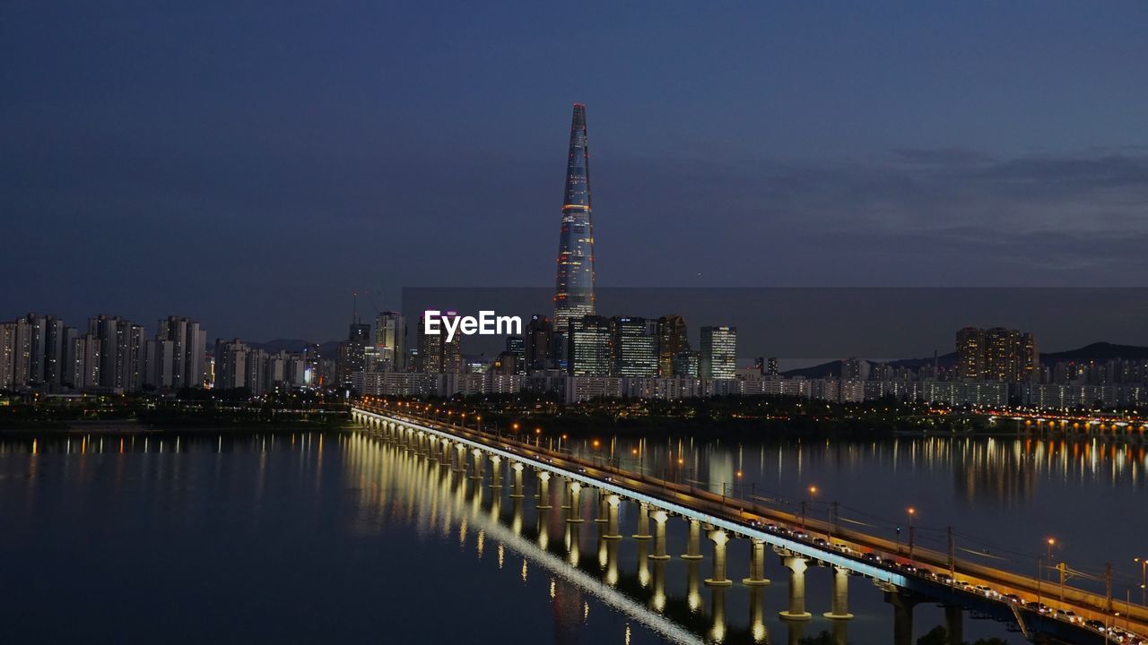 Illuminated buildings by river against sky at night