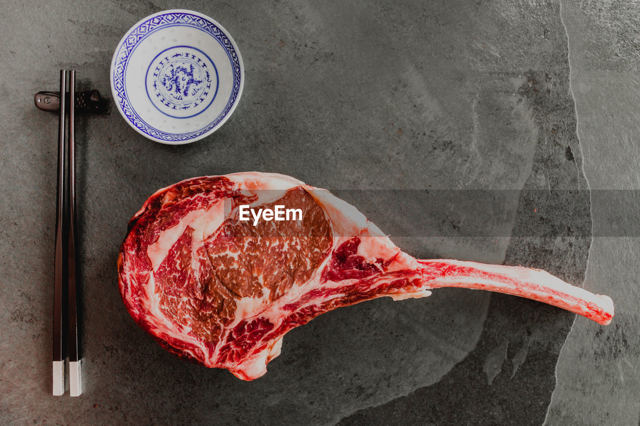 Big sushi. raw, dry-aged wagyu tomahawk steak on a black stone table with chop sticks. top view 