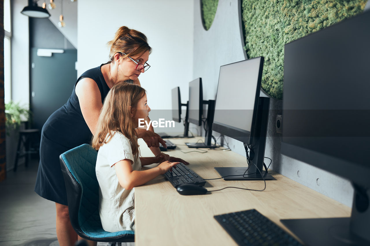 Teacher helping schoolgirl while computer class at primary school. back to school. learning at class