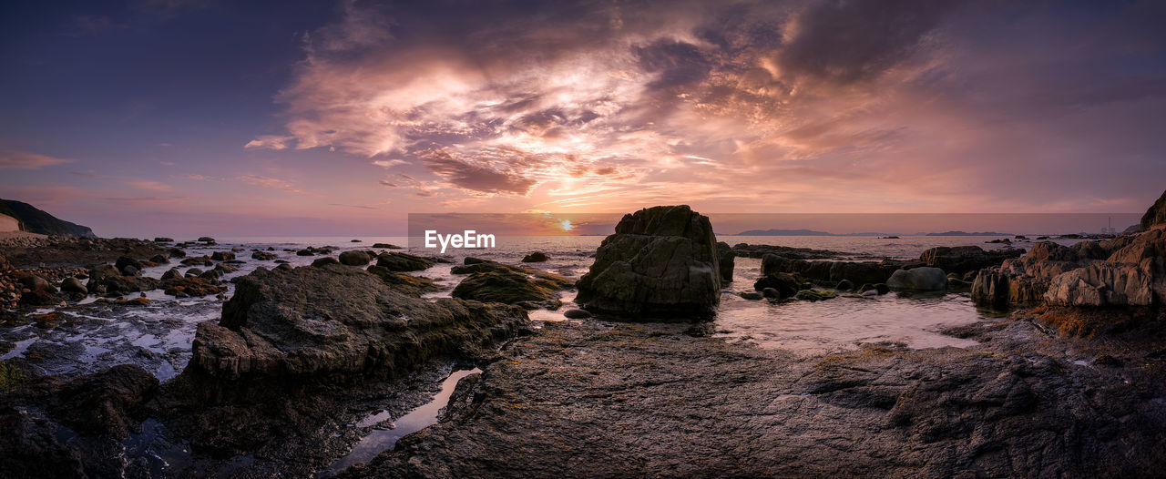 Panoramic view of rocky seashore against sky during sunset