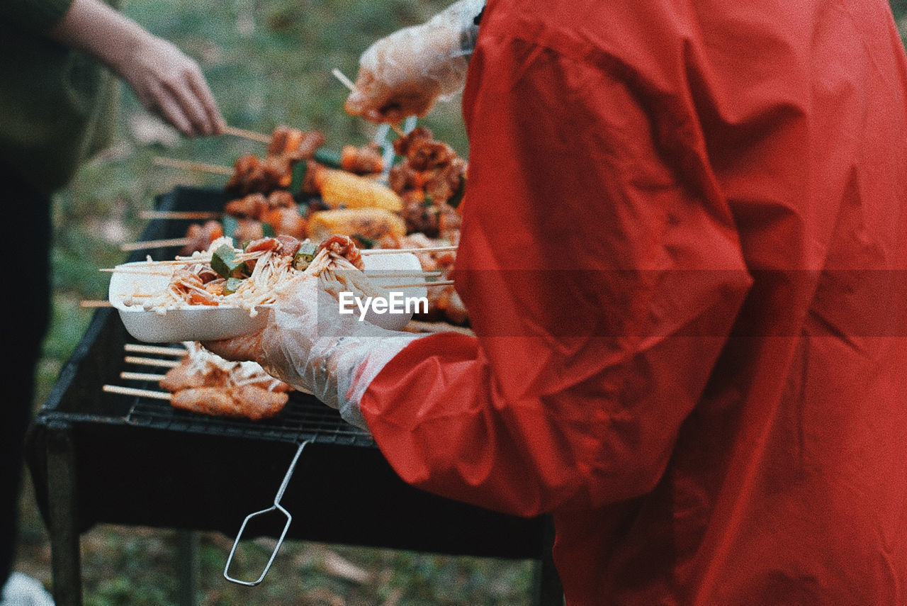 Midsection of person roasting food on barbecue grill