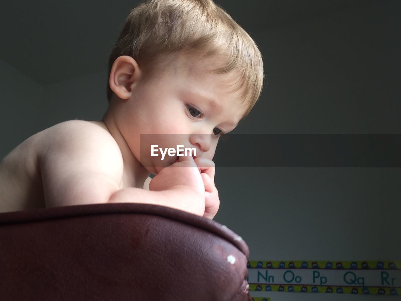 Baby boy looking down while sitting on sofa at home