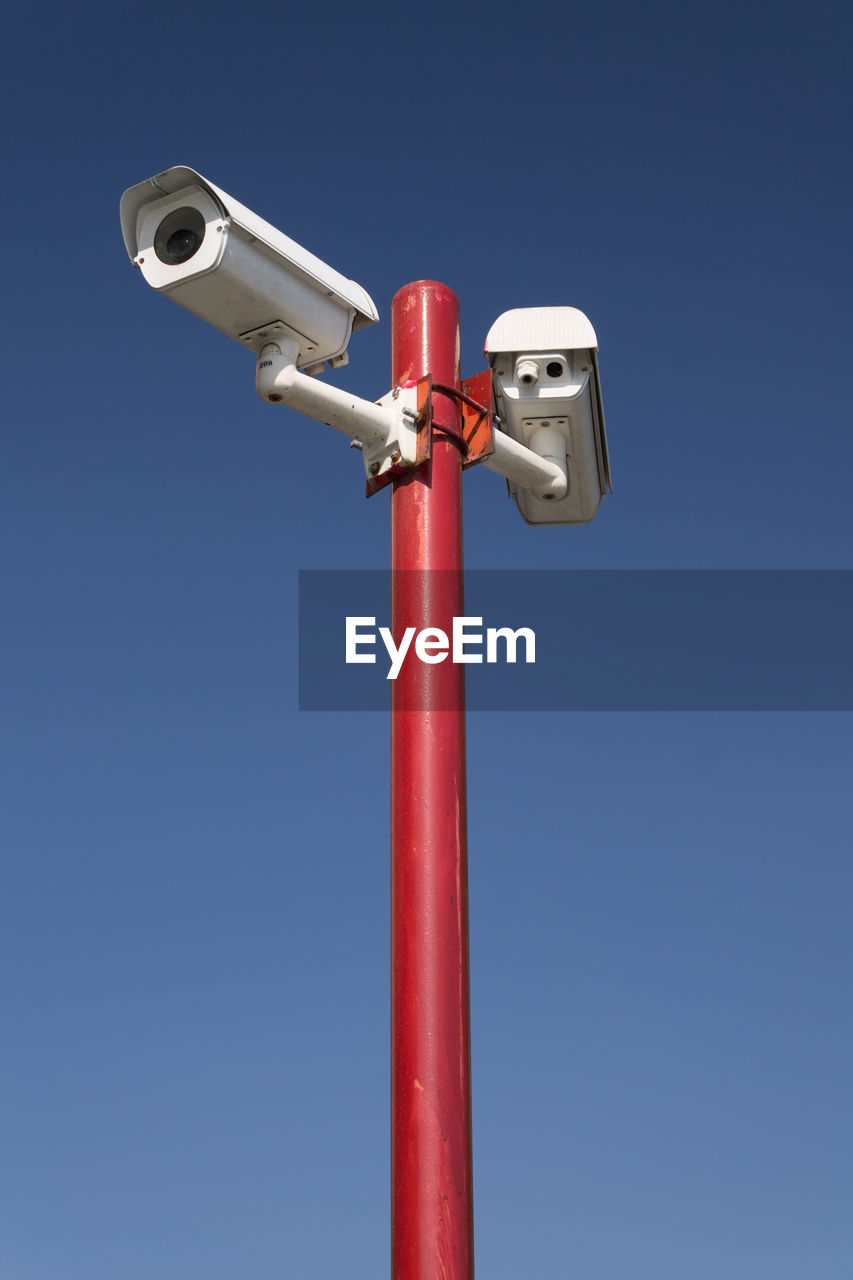 Low angle view of security cameras against clear blue sky