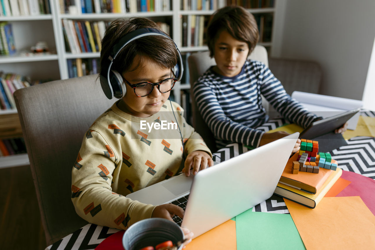 Boy showing laptop to male friend on table at home