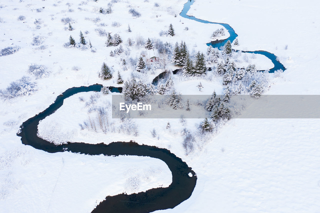 House near river between trees and fields in snow