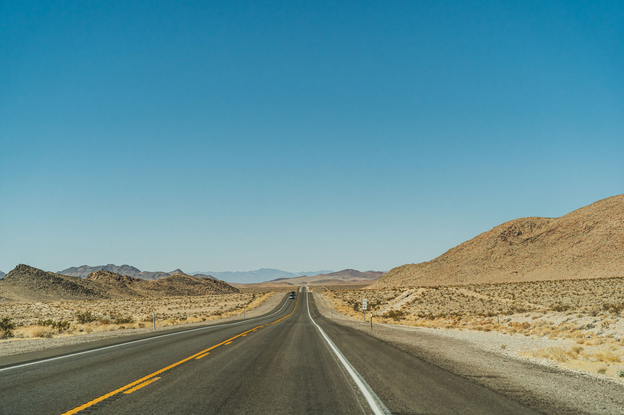 Desert road leading to the horizon against clear blue sky