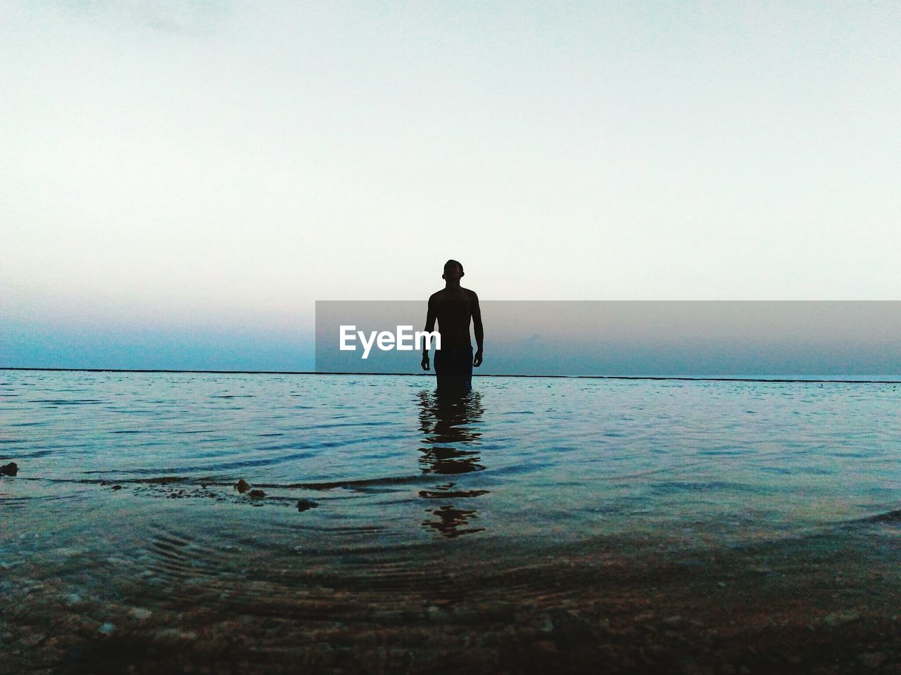 Silhouette man standing in sea against clear sky