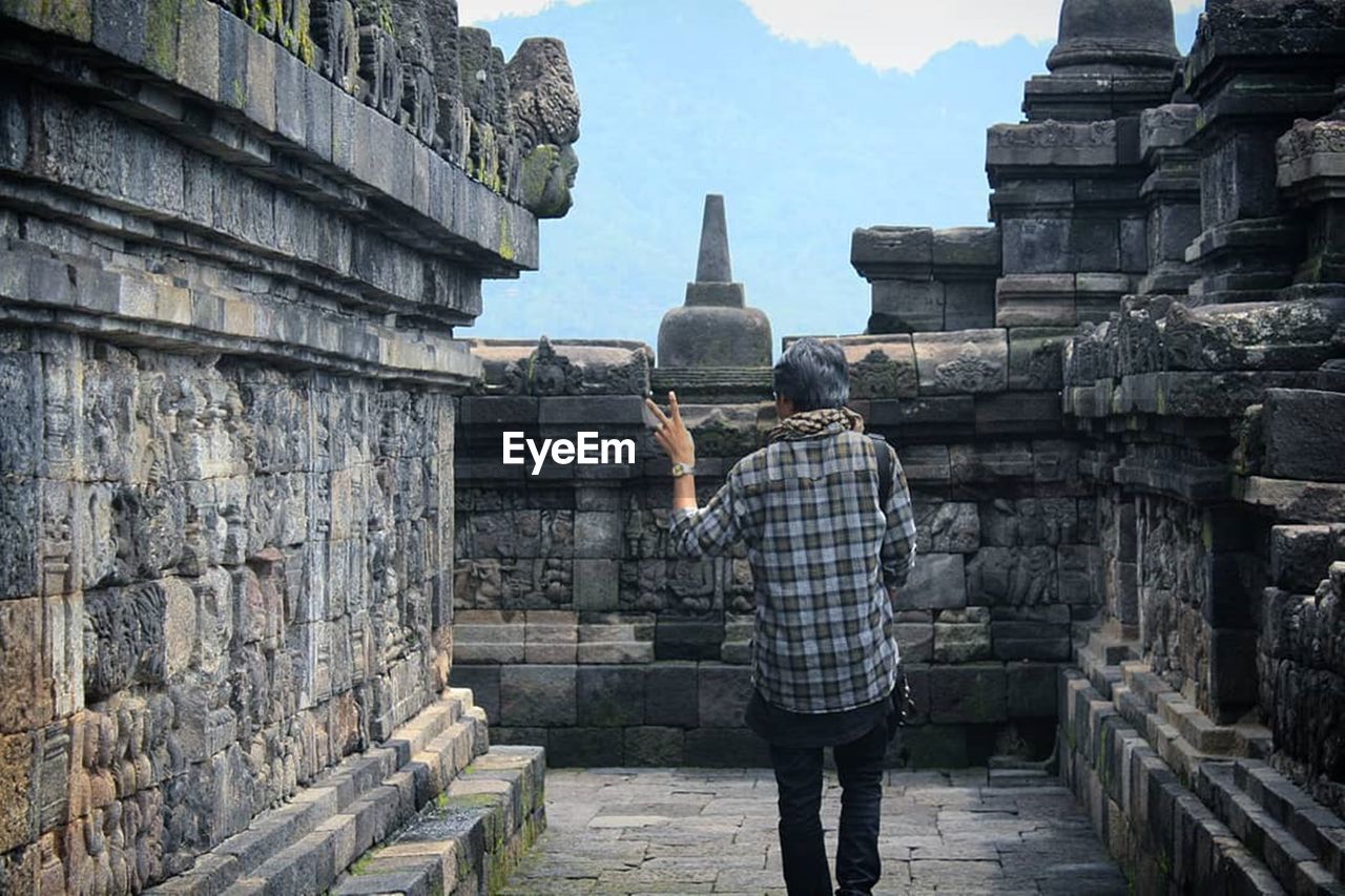 Rear view of person gesturing while walking in temple